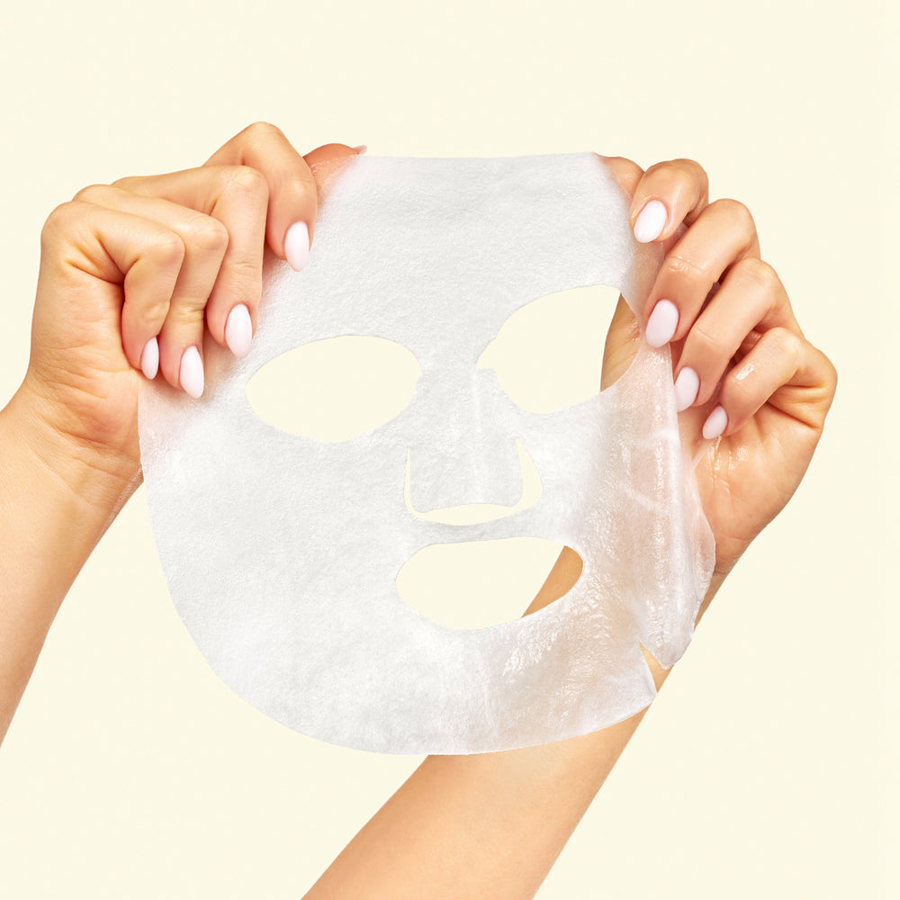 Hands holding a sheet mask against a light background