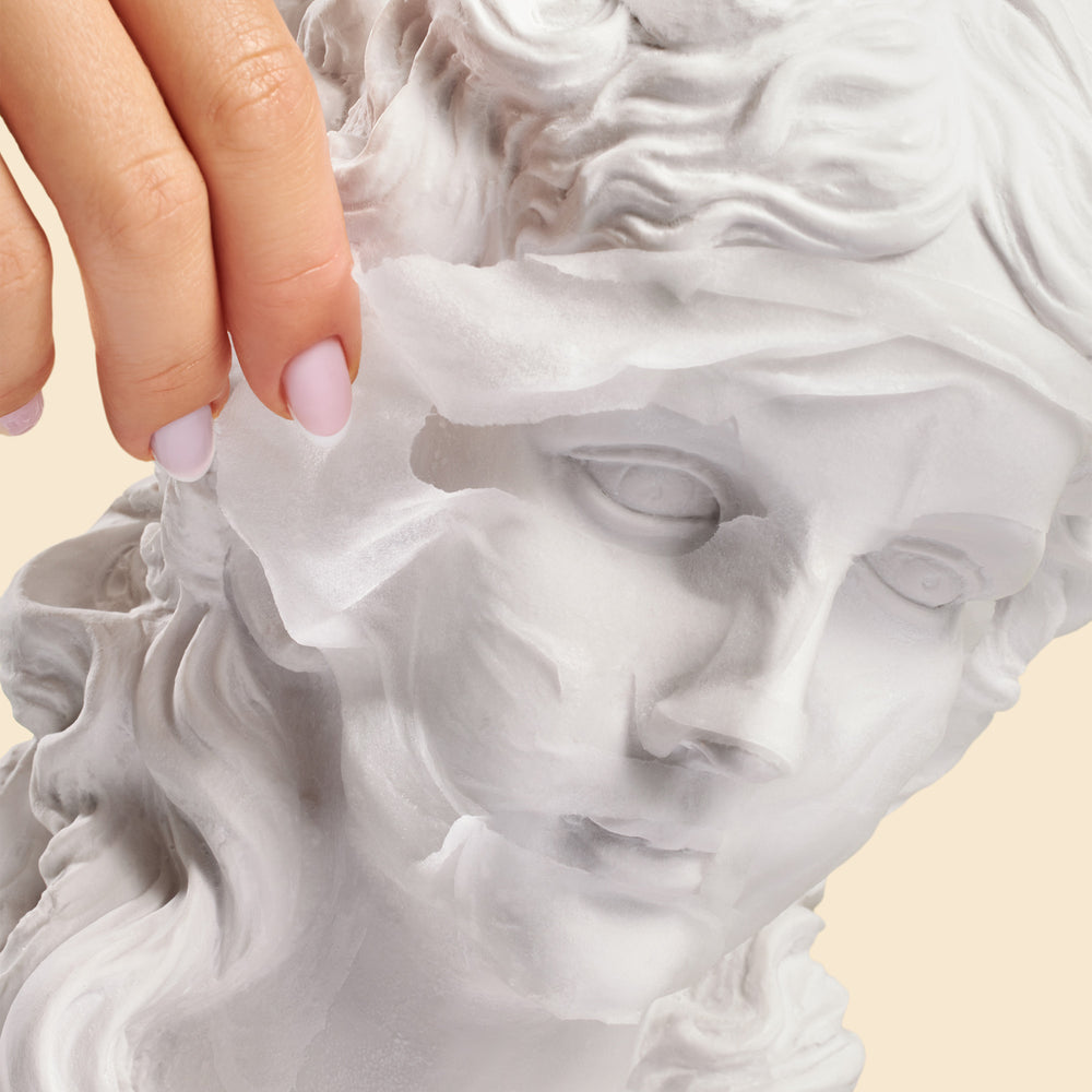 Close-up of a hand touching a marble statue head on a beige background
