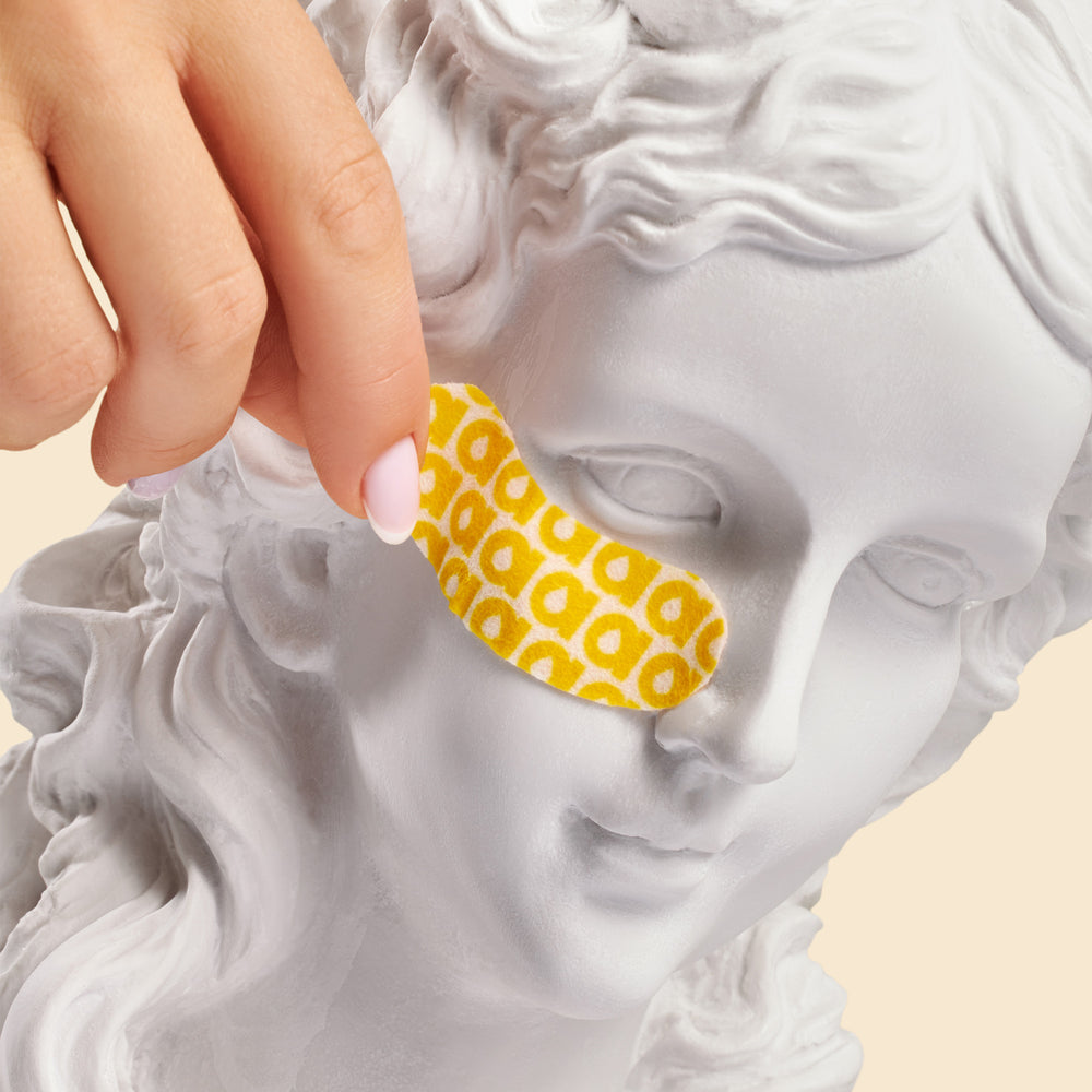 Statue with a yellow bandage on its face, held by a hand.